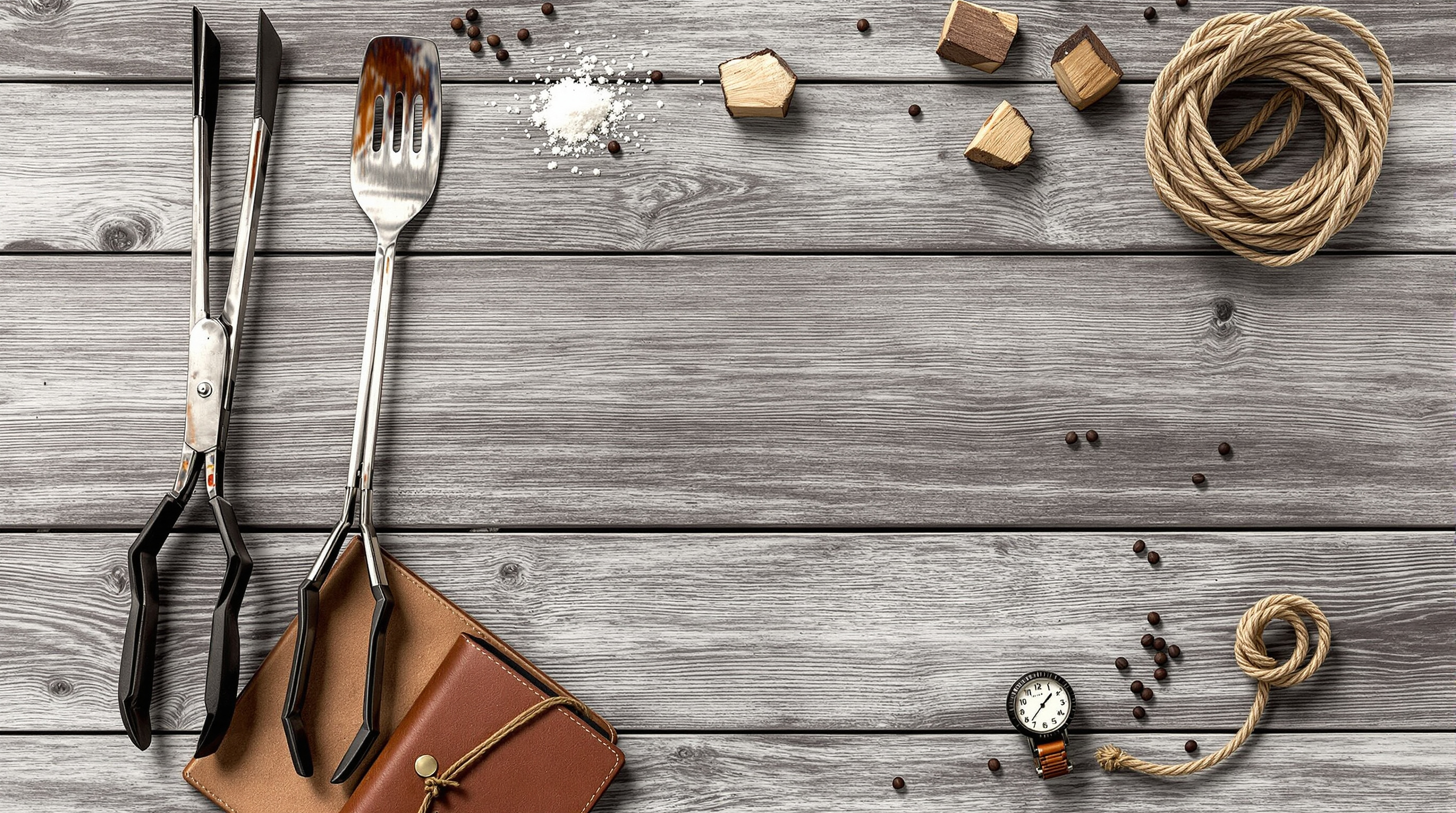 Flat-lay of barbecue tools, a worn recipe notebook, wood chunks and a thermometer on weathered wood